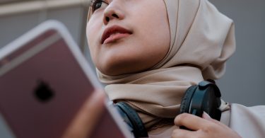 young lady holding pink cellphone wearing headphones on neck