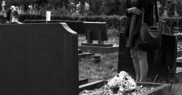 black and white woman standing alone at grave in cemetery mourning