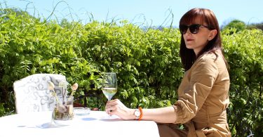 woman in trench coat and sunglasses drinking white wine