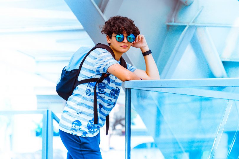 boy wearing blue circle shades leaning pose on glass wall