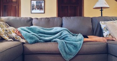 barefoot woman lying on couch with blanket covering her face